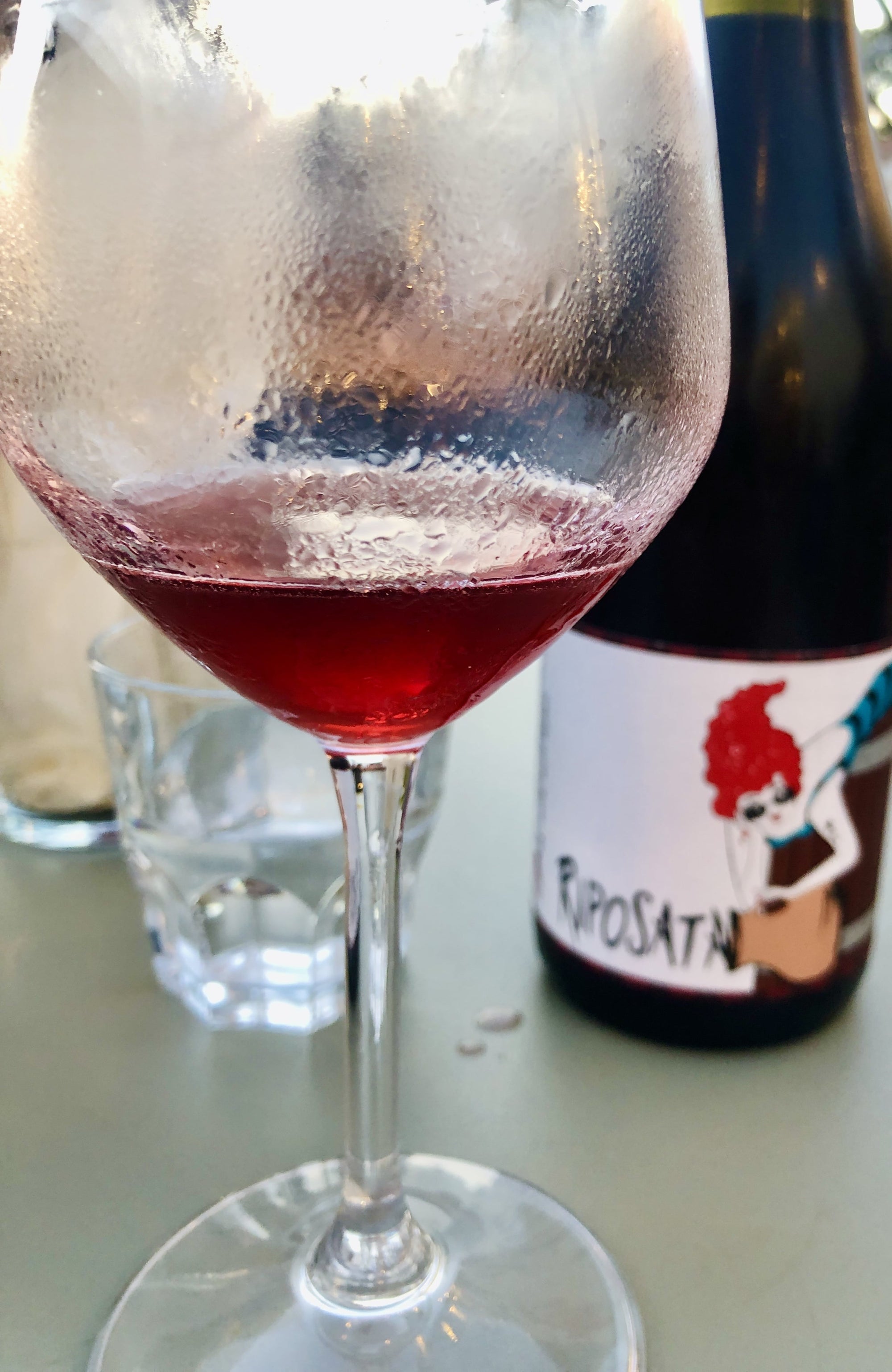 Wine glass with red wine and a bottle labeled 'La Riposata' on a table.