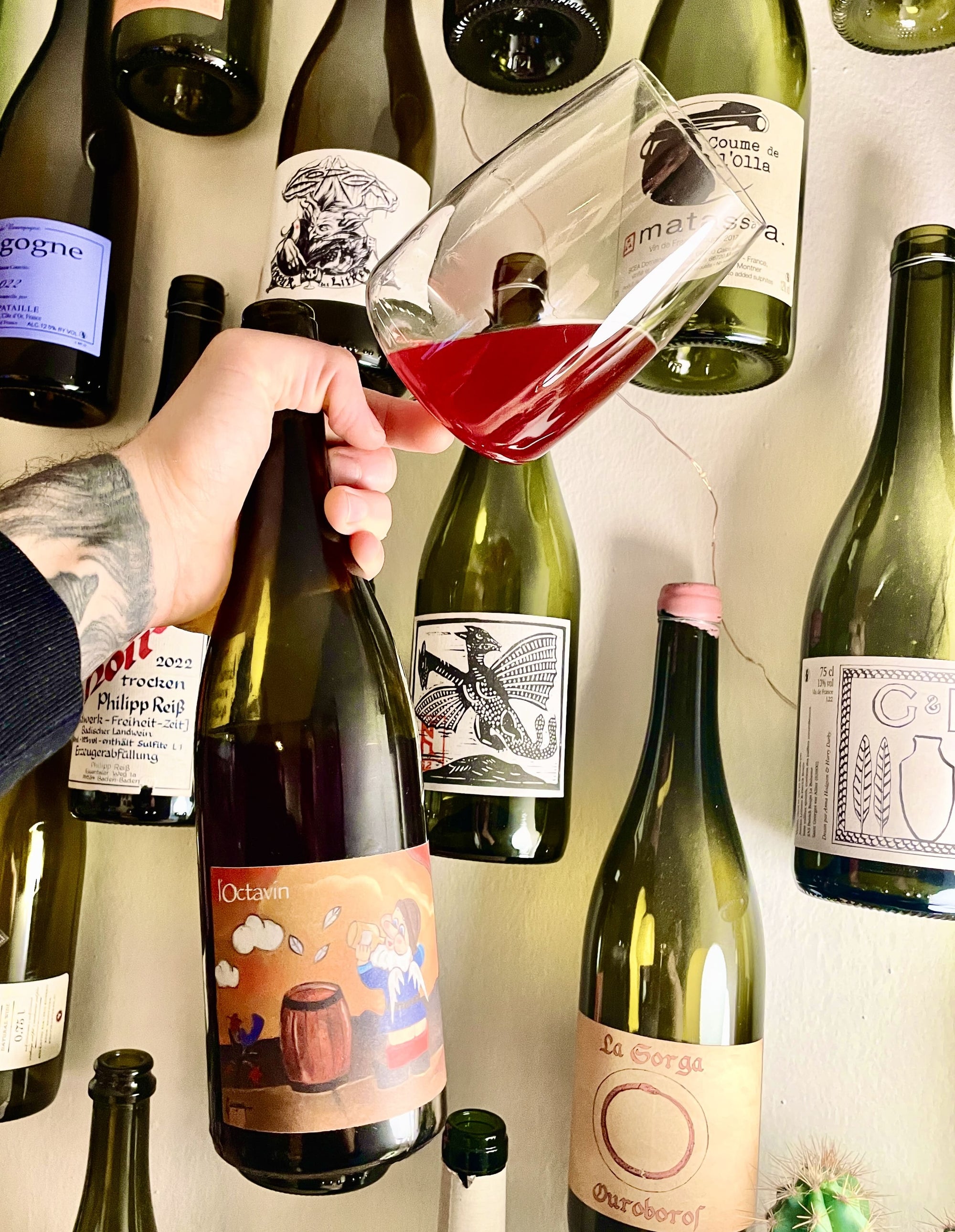 Hand pouring red wine into a glass with wine bottles in the background