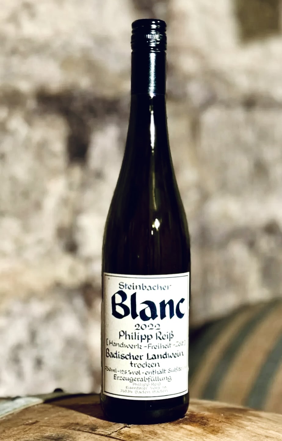 Wine bottle labeled 'Blanc' on a wooden surface with a stone wall background