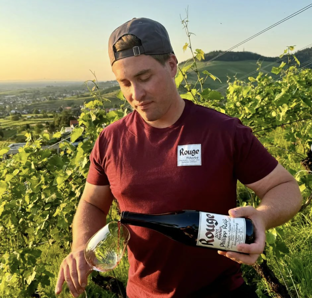 Portrait of winemaker Philipp Reiss in his vineyard with a bottle of Rouge