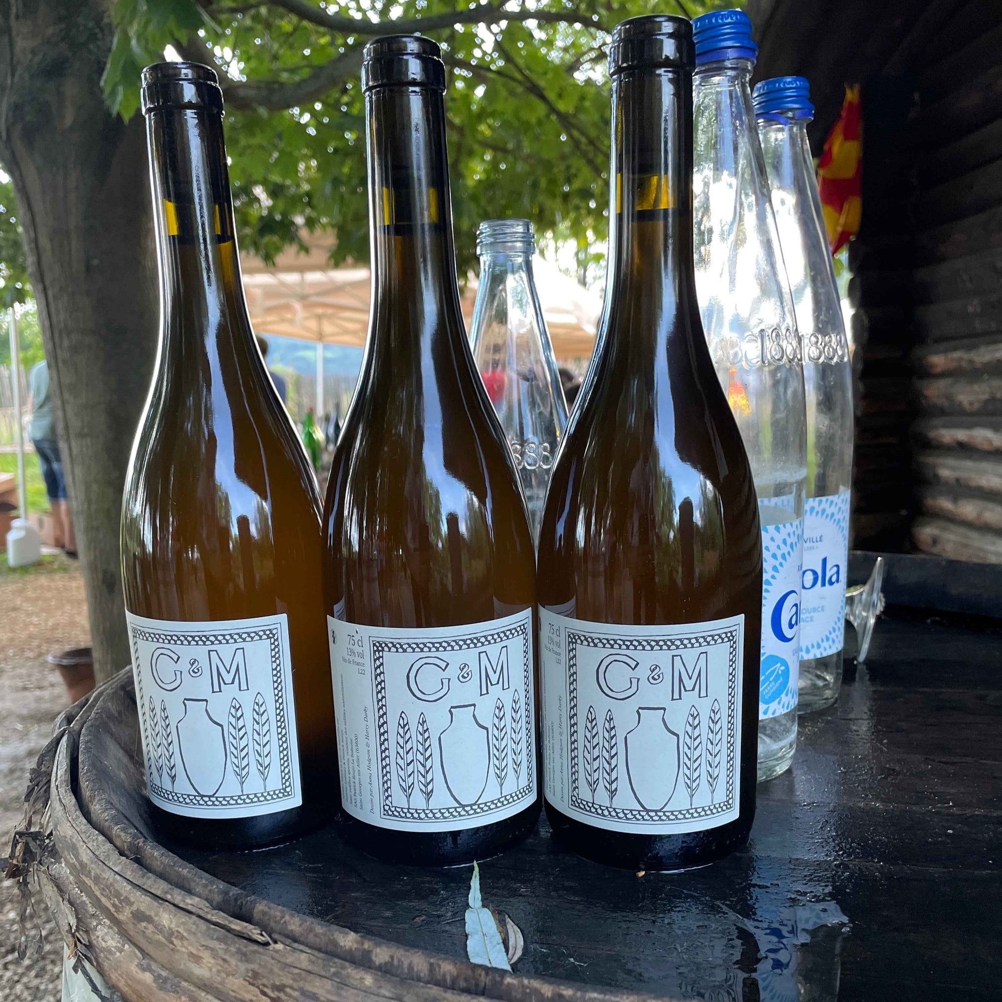 Three wine bottles with labels on a wooden barrel outdoors