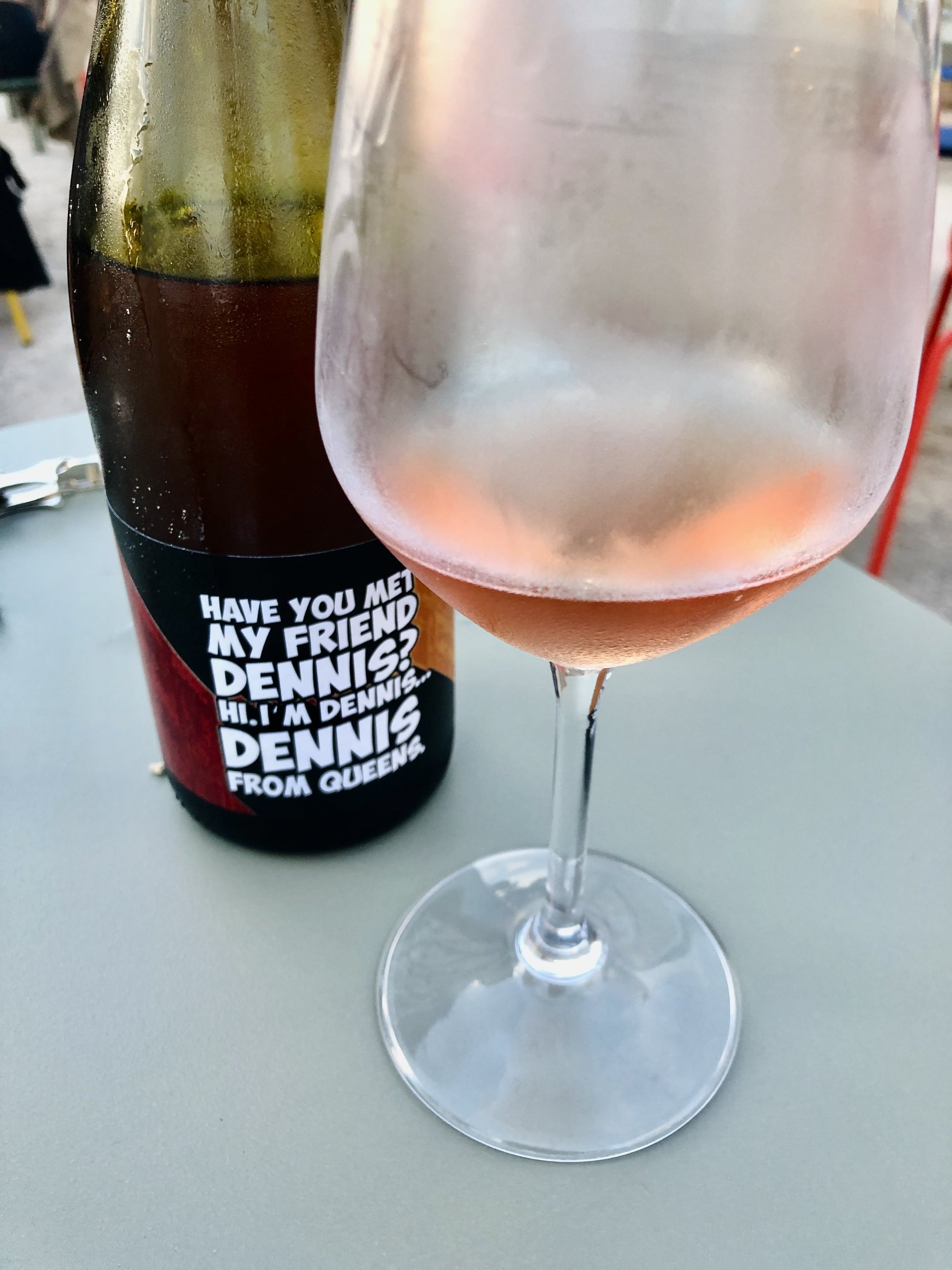 Wine bottle with a humorous label next to a wine glass filled with rosé wine on a table.