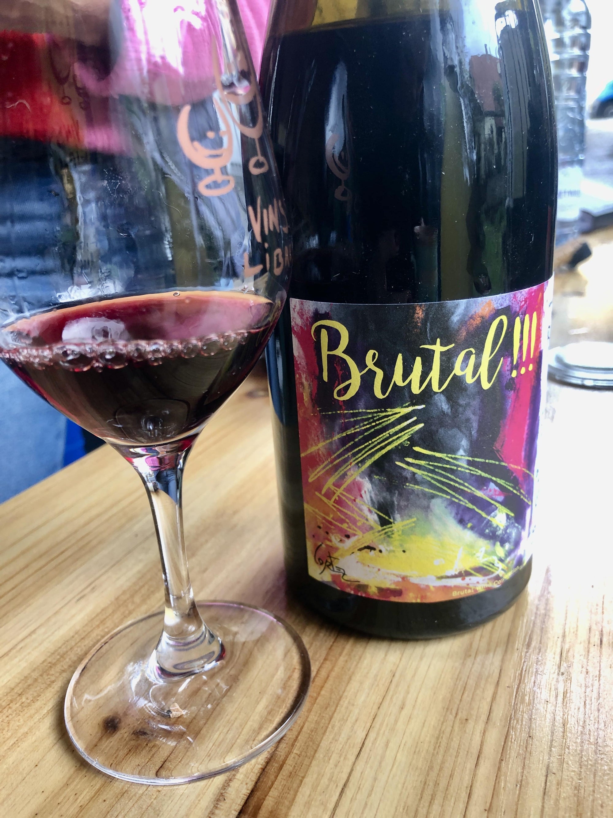 Wine bottle labeled 'Brutal!!!' with a glass of red wine on a wooden surface.