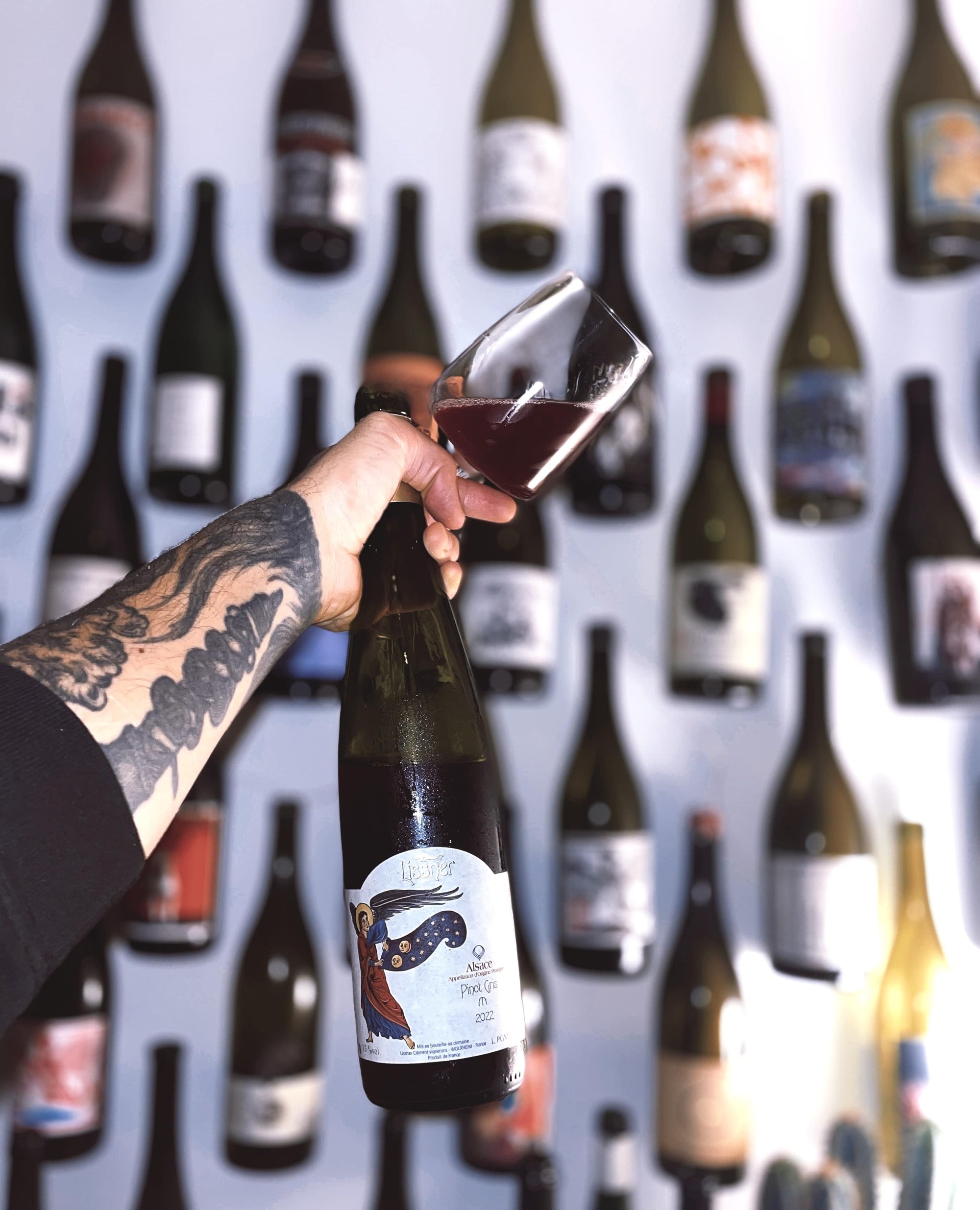 Person pouring wine from a bottle into a glass with a background of wine bottles.