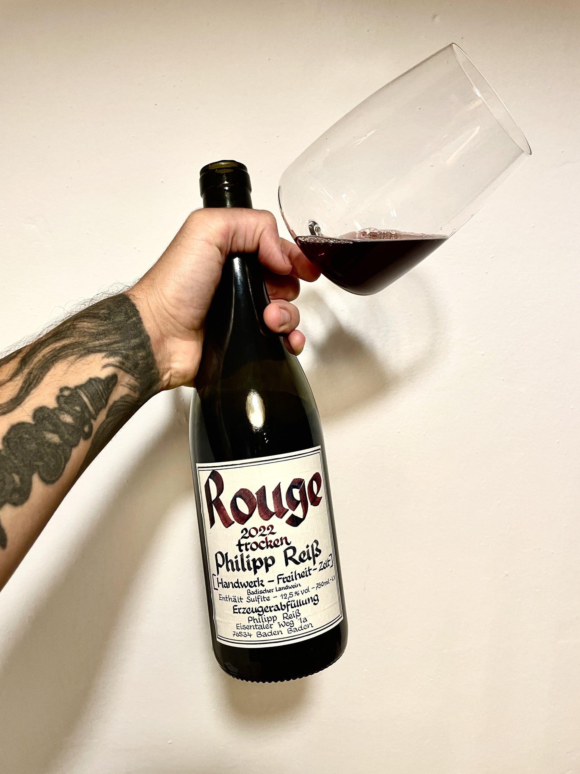 A bottle and a glas of red wine with a label saying Rouge on neutral background