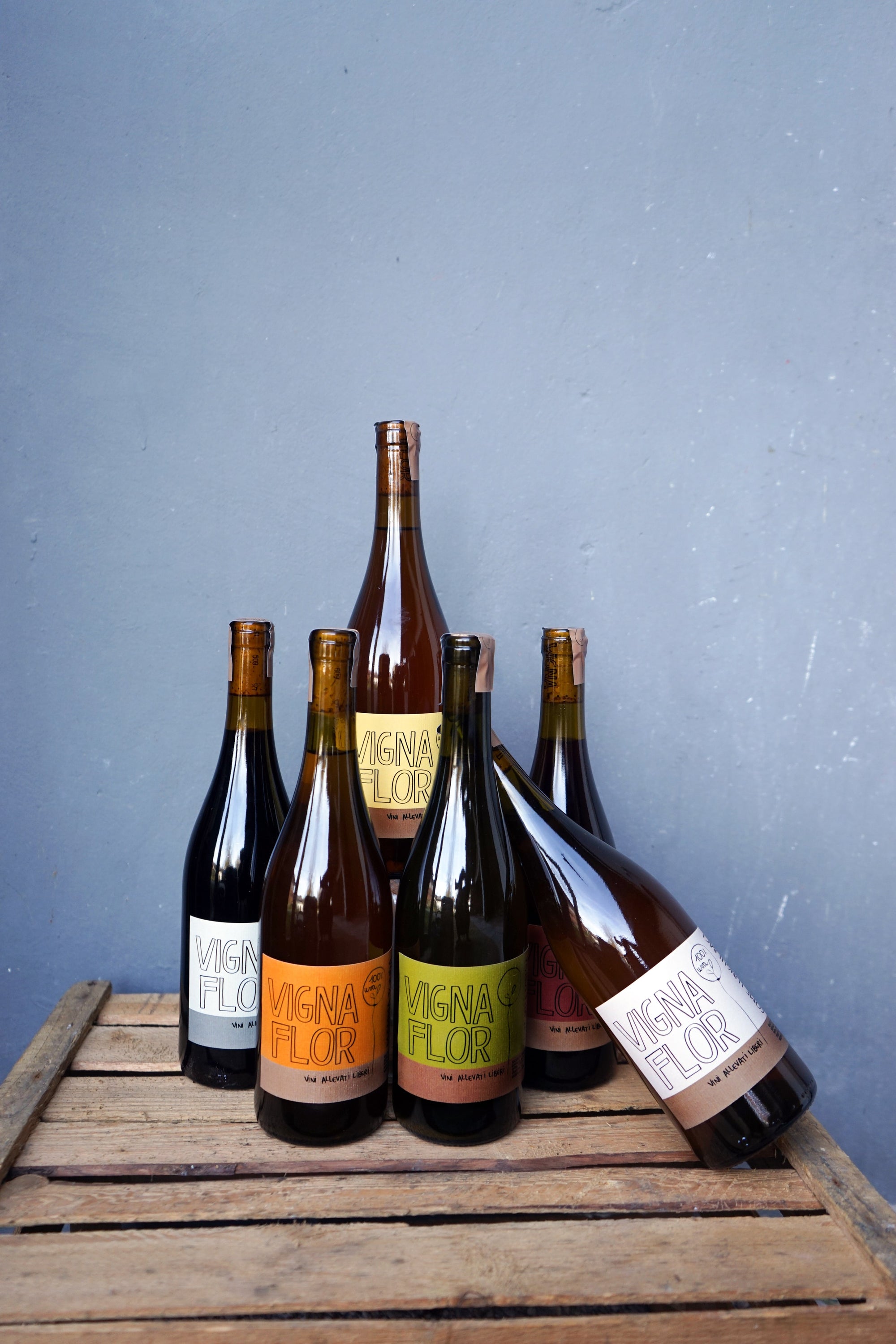 Collection of natural wine bottles on a wooden crate with a blue background